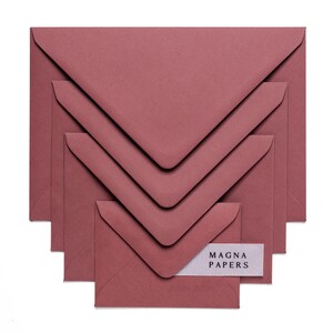 May include: Set of five burgundy envelopes of different sizes, stacked on top of each other. The smallest envelope has a white label with the text "MAGNA PAPERS" printed on it.