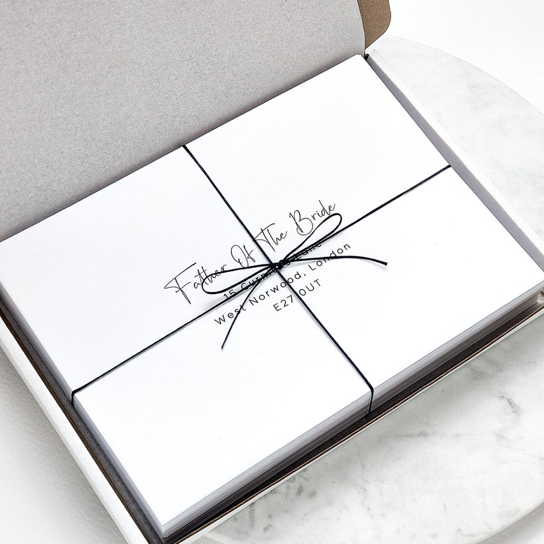 May include: A stack of white cards tied with black string. The cards have the text "Father of the Bride" and an address printed on them.