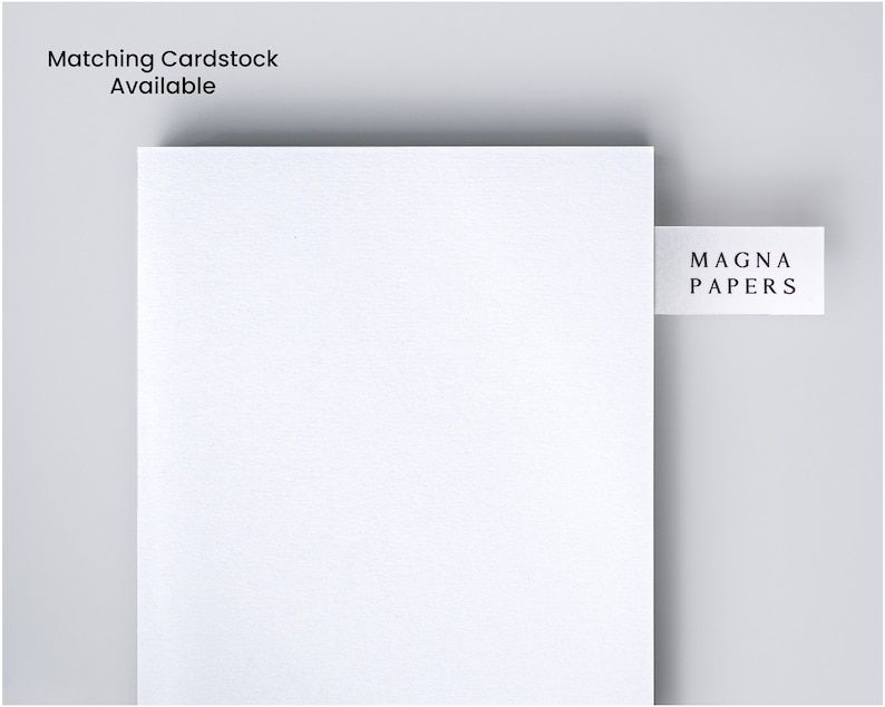 May include: A white sheet of paper with a textured surface. The paper has a small white label attached to the top right corner with the text "MAGNA PAPERS" printed in black.