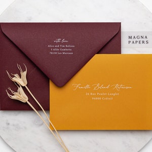 May include: Two envelopes, one burgundy and one mustard yellow, with white calligraphy addressing them. The burgundy envelope has the text "with love" and the mustard yellow envelope has the text "Famille Boland Retaruson". The text "MAGNA PAPERS" is visible on a clear sticker.