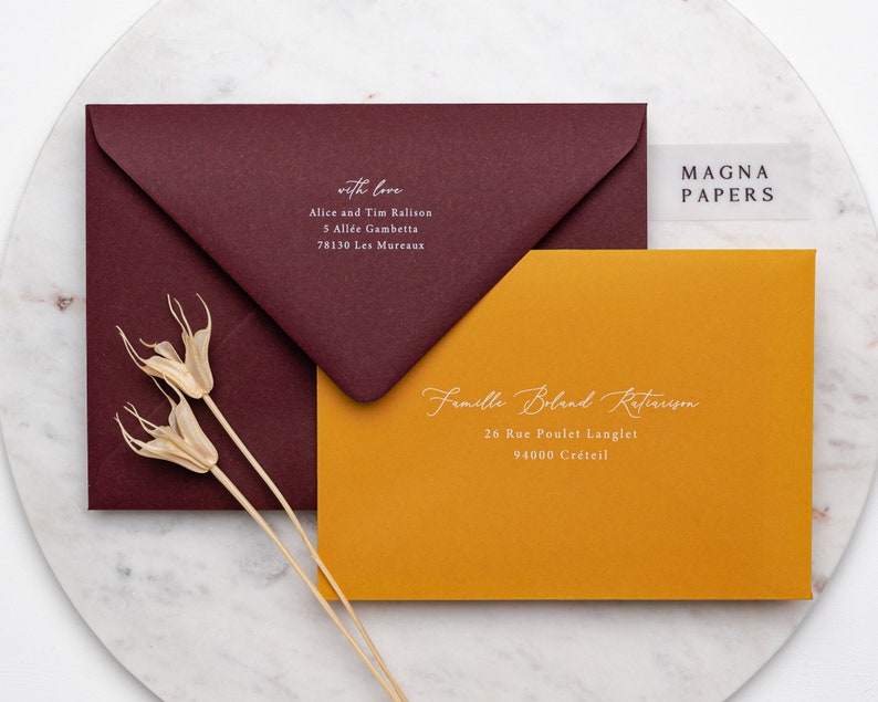 May include: Two envelopes, one burgundy and one mustard yellow, with white calligraphy addressing them. The burgundy envelope has the text "with love" and the mustard yellow envelope has the text "Famille Boland Retaruson". The text "MAGNA PAPERS" is visible on a clear sticker.