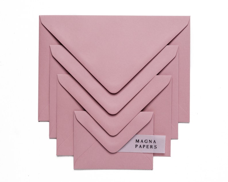 May include: A set of five dusty rose envelopes of varying sizes, nested inside each other. The smallest envelope has a white label with the text "MAGNA PAPERS" printed in black.