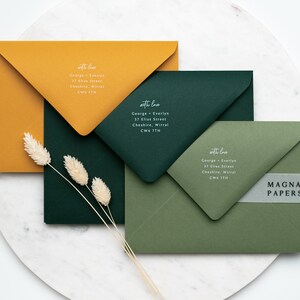 May include: Three envelopes in different colors: mustard yellow, forest green, and olive green. Each envelope has a white handwritten address label with the text "with love" and a name and address. The bottom envelope has a clear sticker with the text "MAGNA PAPERS" in black.