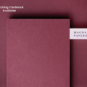 May include: A close-up of a deep burgundy cardstock sample with a white label that reads "MAGNA PAPERS".