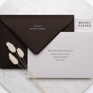 May include: A light grey envelope with a white address label that reads "MRS AND MRS SPENCER 96 RALEIGH COURT LYMER AVENUE SE19 3GS". The envelope is sitting on a white marble surface with a brown envelope and dried flowers.