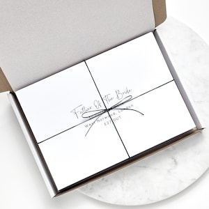 May include: A white box with a black ribbon tied around it. The box is labelled "Father of the Bride" with an address in West Norwood, London, E27 OUT.