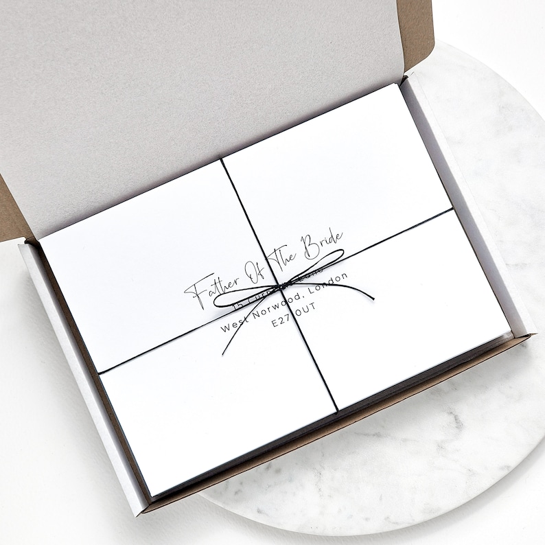 May include: A white box with a black ribbon tied around it. The box is labelled "Father of the Bride" with an address in West Norwood, London, E27 OUT.
