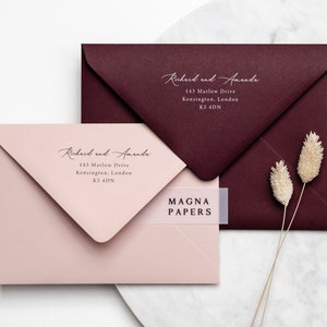May include: Two envelopes, one burgundy and one blush pink, with the text "Richard and Amanda" and their address printed on them. The burgundy envelope has a white label with the text "MAGNA PAPERS" on it.