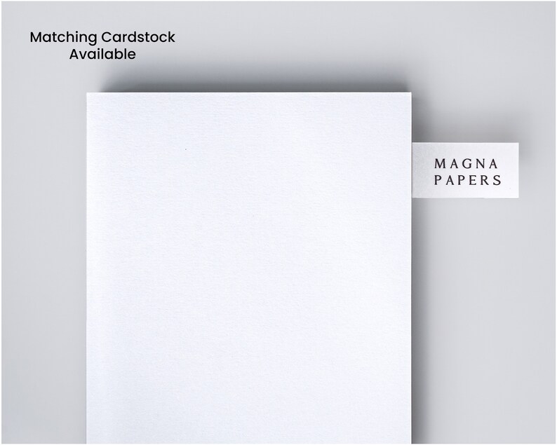 Puede incluir: Primer plano de un papel de cartulina blanca con el texto "Matching Cardstock Available" en la esquina superior izquierda. Una peque&ntilde;a etiqueta blanca con el texto "MAGNA PAPERS" est&aacute; adjunta al lado derecho del papel. El fondo es gris claro.