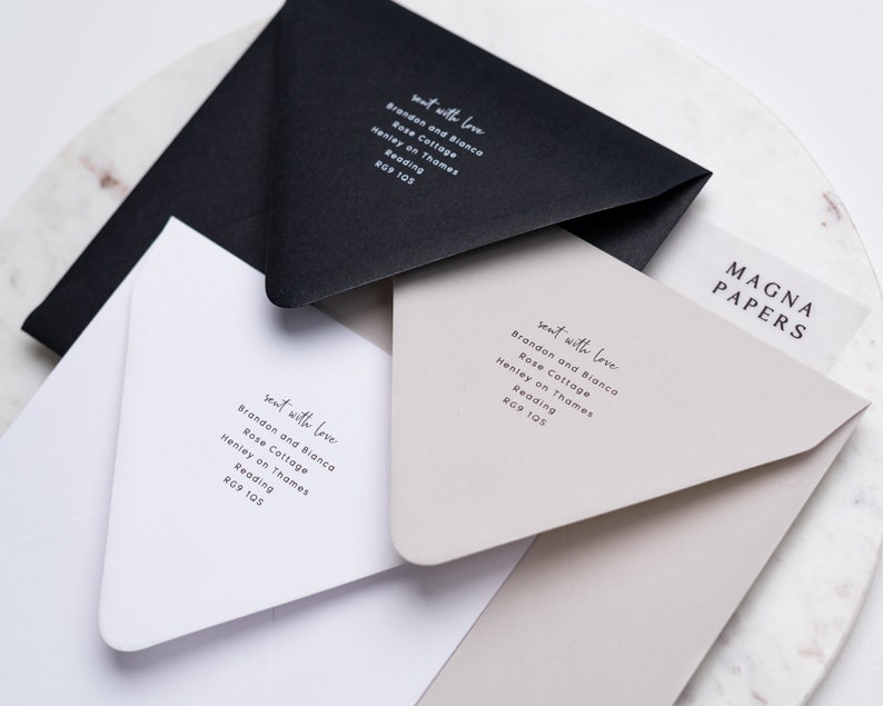 May include: Three white envelopes with black text on them. The text reads "sent with love" followed by the address "Brandon and Bianca, Rose Cottage, Henley on Thames, Reading, RG9 105". The envelopes are stacked on top of each other. The top envelope is a light beige colour. The bottom envelope is white. The middle envelope is black. The envelopes are on a white marble surface. The text "MAGNA PAPERS" is visible in the top right corner of the image.