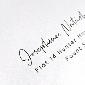 Puede incluir: Primer plano de un papel blanco con texto manuscrito negro. El texto incluye el nombre "Josephine, Natasha" en escritura cursiva, seguido de una direcci&oacute;n: "Flat 14 Hunter House, Fount S". El papel tiene una superficie texturizada.