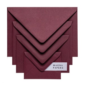 May include: Set of five burgundy envelopes of different sizes, stacked on top of each other. The smallest envelope has a white label with the text "MAGNA PAPERS" printed on it.