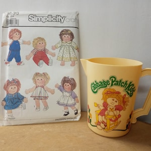 May include: A vintage Simplicity sewing pattern for Cabbage Patch Kids dolls. The pattern is for making clothes for the dolls. The pattern is on a white background with a green and white border. The pattern is for sizes 12-18 months. The pattern is in good condition. There is also a yellow pitcher with a Cabbage Patch Kids logo and a picture of a doll sitting in a rocking chair.