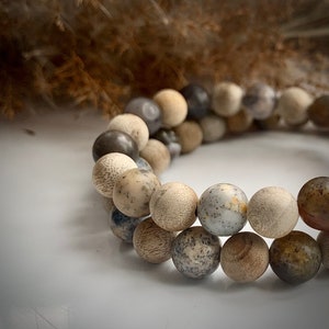 May include: A bracelet made of brown, grey, and white beads. The beads are round and have a natural, earthy look.