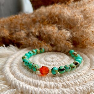 May include: A turquoise and gold beaded bracelet with a single orange gemstone accent.