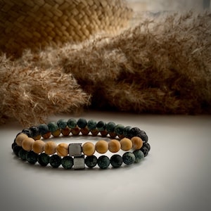 May include: Two stacked bracelets, one with green and black beads and the other with light brown beads. The bracelets have silver metal accents.