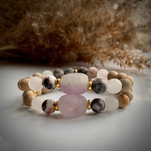Peut inclure: Deux bracelets avec des perles en bois, des perles d'agate blanches et grises, et deux grosses perles de couleur lavande.