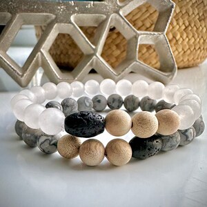 May include: Two bracelets made of natural stones. One bracelet is made of white and grey stones, the other is made of brown and black stones. The bracelets are stacked on top of each other.