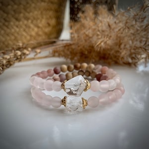 May include: Two bracelets with pink and brown beads and a clear crystal charm with gold accents.