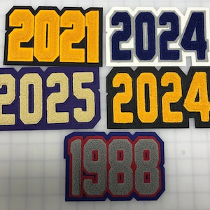 以下が含まれることがあります： 異なる色の背景と数字を持つ5つのフェルトパッチ。数字は2021、2024、2025、2024、1988です。