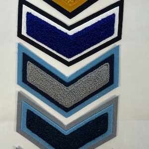 以下が含まれることがあります： さまざまな色のシェブロン型のパッチのコレクション。パッチは、黄色、青、グレー、ネイビーの色合いの、フェルトのような質感の素材でできており、黒と白の縁取りが施されています。これらのパッチは、装飾または識別目的である可能性があります。