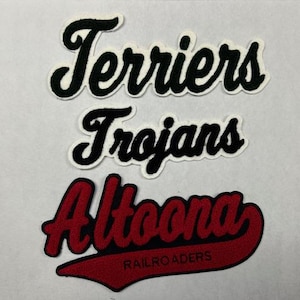 以下が含まれることがあります： 白い生地に黒い文字で刺繍された3つのパッチ。一番上のパッチには「Terriers」、真ん中のパッチには「Trojans」、一番下のパッチには赤と黒のパッチに赤い文字で「Altoona Railroaders」と書いてあります。