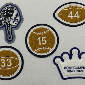 以下が含まれることがあります： 金色の背景と白いステッチで刺繍された5つのパッチ。パッチには、15番の野球、33番のバスケットボール、44番のフットボール、ネイティブアメリカンの頭、そして「HOMECOMING KING 2024」というテキストが書かれた王冠が含まれています。