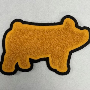 Könnte beinhalten: Ein goldener Schweine-Silhouetten-Patch mit schwarzem Umriss. Der Patch ist aus einem flauschigen Material.