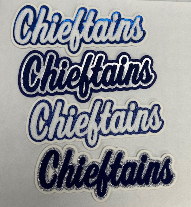 May include: Four die-cut iron-on patches featuring the word Chieftains in a cursive script font. The patches display various color combinations of blue, white, and silver glitter textures with layered outlines and a white border.