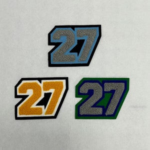 May include: Three felt patches with the number 27 in different colors. The patches are gray with black trim, yellow with black trim, and green with blue trim.