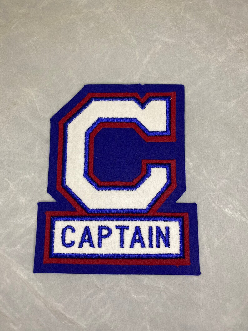 May include: A blue and red felt patch with a white felt letter "C" and the word "CAPTAIN" in white felt.