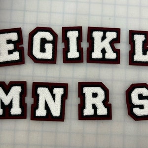 以下が含まれることがあります： 白のフェルト文字で書かれた、ワインレッドのフェルトレターパッチのセット。文字はE、G、I、K、L、M、N、R、Sです。