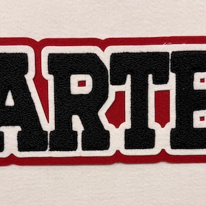 May include: A fabric patch featuring the name CARTER in bold black block letters. The lettering is outlined in a thick white border, which is then surrounded by a vibrant red background layer that follows the contour of the text.