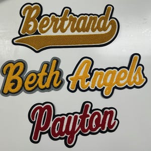 以下が含まれることがあります： 4つの名前が刺繍されたパッチ。「Bertrand」は金と黒、「Beth」は金とグレー、「Angels」は金と黒、「Payton」は赤と黒。パッチはカレッジ風の文字スタイルです。