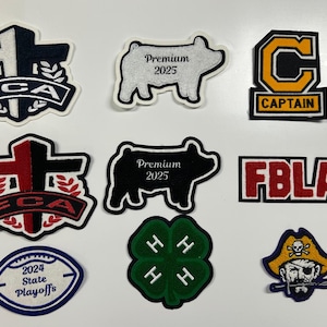 以下が含まれることがあります： さまざまな形と色をした刺繍パッチのコレクション。デザインには、十字架、「Premium 2025」の豚、「CAPTAIN」の「C」、「FBLA」、「2024 State Playoffs」のフットボール、四つ葉のクローバー、海賊が含まれています。