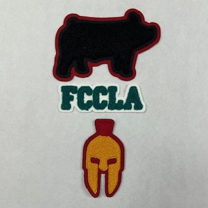 以下が含まれることがあります： 刺繍された3つのパッチ: 豚の黒いシルエット、FCCLAという文字の入った緑のパッチ、赤と黄色のスパルタのヘルメット。