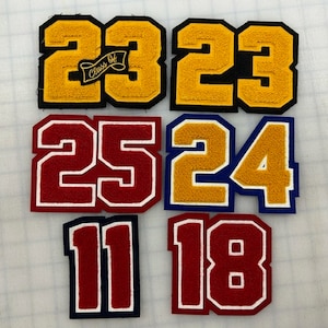 以下が含まれることがあります： 卒業年の数字が書かれたフェルトパッチ6枚。パッチは赤、黄、青で、白い縁取りがされています。一番上のパッチは黄色で、数字は2023、バナーには「Class of」と書いてあります。他のパッチは25、24、11、18です。