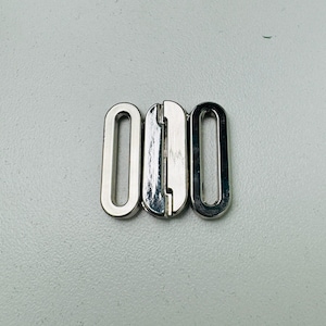 May include: Silver metal slider buckle with three oval-shaped pieces. The buckle is designed to be used for straps or belts.