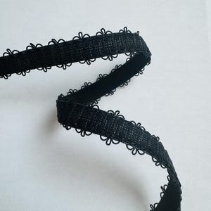 May include: A length of black lace trim with a scalloped floral edge. The trim is made of a woven material and is shown against a white background. This decorative trim is suitable for sewing and craft projects.