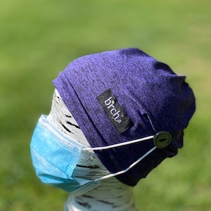 May include: Purple and black patterned beanie with a white elastic band and a black button. The beanie has a small black label with the word "birch" on it.