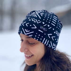 May include: A black and white patterned beanie with a white logo that says "birch" on the side. The beanie is worn by a person with dark hair and a nose ring.