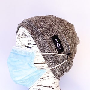May include: Gray and white knit beanie with a button on the side and a white elastic strap. The beanie has a label that says "birch" on it. A light blue face mask is attached to the strap.