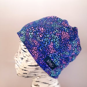 May include: A blue, pink, and turquoise beanie with a leopard print pattern. The beanie has a black label with the text "brch.se" on it.