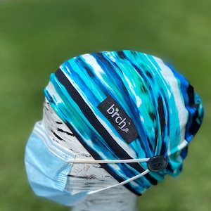 May include: A blue and white striped fabric headband with a button on the side. The headband has a black label with the word "birch" on it.