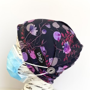 May include: A black beanie with a floral print in shades of purple and pink. The beanie has a button on the side for attaching a face mask. The brand name "brchz" is visible on the beanie.