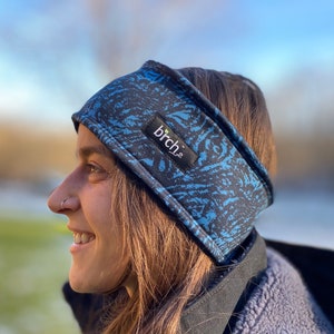 Puede incluir: Una diadema de color azul y negro con estampado y la palabra "birch" impresa. La diadema la lleva puesta una persona con el pelo largo y castaño.