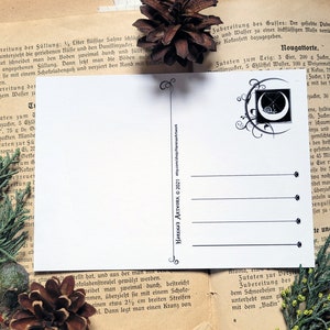 May include: A white postcard with a black and white illustration of a crescent moon with a cross inside. The illustration is surrounded by a decorative border. The text "HARENA'S ARTWORK &copy; 2021" is printed in black at the bottom right corner of the postcard.