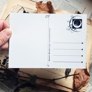May include: A white postcard featuring a black and white illustration of a crescent moon with a snail inside. The moon is surrounded by a decorative floral design. The text "HARENA'S ARTWORK &copy; 2021 etsy.com/shop/HarenasArtwork" is printed on the back of the postcard.