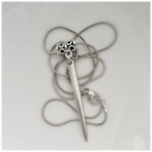 May include: A silver necklace featuring a long, pointed pendant. The pendant is attached to a silver chain with an ornate clasp.