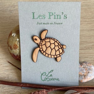 Peut inclure: Épingle en bois en forme de tortue sur une carte grise avec le texte "Les Pin's Fait main en France" et "La Cocornerie". L'épingle est marron clair avec un motif de carapace détaillé. La carte est sur une surface en bois.